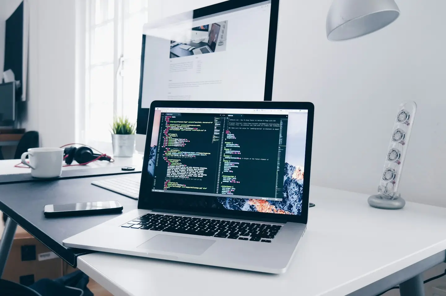 Laptop with code on a clean white desk beside a lamp